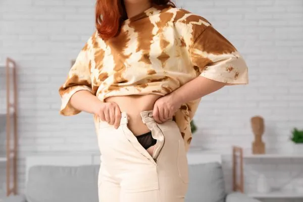 Image of woman trying to do her trousers up after pregnancy weight gain Chester